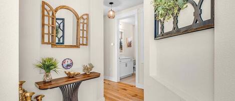 Un pasillo con una consola de madera, espejos decorativos y una planta colgante.