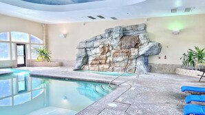 Una piscina con un muro de piedra y sillas de descanso azules.