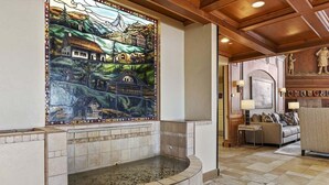 Un área de spa con una pared de mosaicos, una bañera de piedra y una sala de estar con un sofá y una estatua.