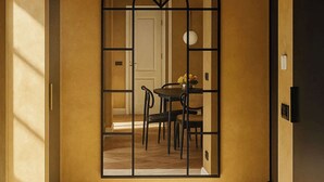 Un pasillo con un espejo arqueado grande, un comedor con mesa y sillas, y una puerta a la derecha.