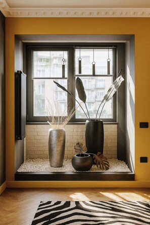 A room with a large window, a radiator, a zebra-patterned rug, and two decorative vases with plants.