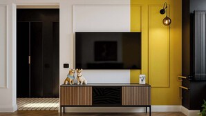 A modern living room with a large flat-screen TV mounted on a white wall, a wooden console table with decorative items, and a yellow accent wall.