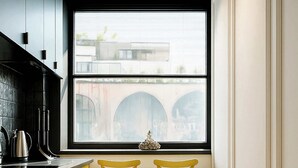 A kitchen with yellow cabinets, a black countertop, and a window with a view of a bridge. There are two yellow chairs at a small table.
