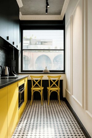 A kitchen with yellow cabinets, a black countertop, and a window with a view of a bridge. There are two yellow chairs at a small table.