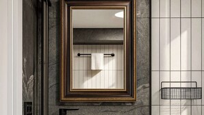 Une salle de bain moderne avec un lavabo en marbre, un miroir encadré d’or et des meubles de rangement noirs.