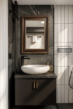 A modern bathroom with a marble sink, a gold-framed mirror, and black cabinetry.