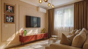 A living room with a TV, a red console, a beige sofa, and a large window with curtains. - Qult·co - Huxley (București)