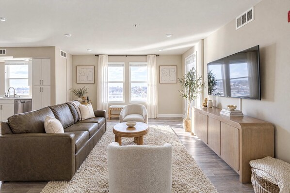 A modern living room with a leather sofa, a round coffee table, and a flat-screen TV mounted on the wall. - Sparks Marina 2BR · Waterfront Views & Rooftop (Sparks)