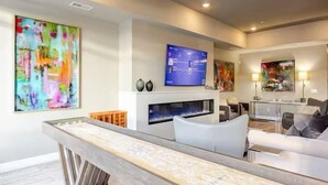 A modern living room with a flat-screen TV mounted above a fireplace, surrounded by contemporary furniture and abstract art. - Sparks Marina 2BR · Waterfront Views & Rooftop (Sparks)