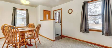 A dining room with a wooden table and chairs, a ceiling light, and a door leading to another room.