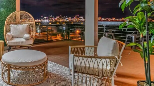 Une terrasse sur le toit, meublée de mobilier en osier, offrant une vue sur le paysage urbain illuminé la nuit, et agrémentée d’un mur végétal.