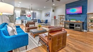 Un salon moderne avec un canapé bleu, un fauteuil en cuir marron et une table basse. Un téléviseur est fixé au mur et un ventilateur de plafond est installé au plafond.