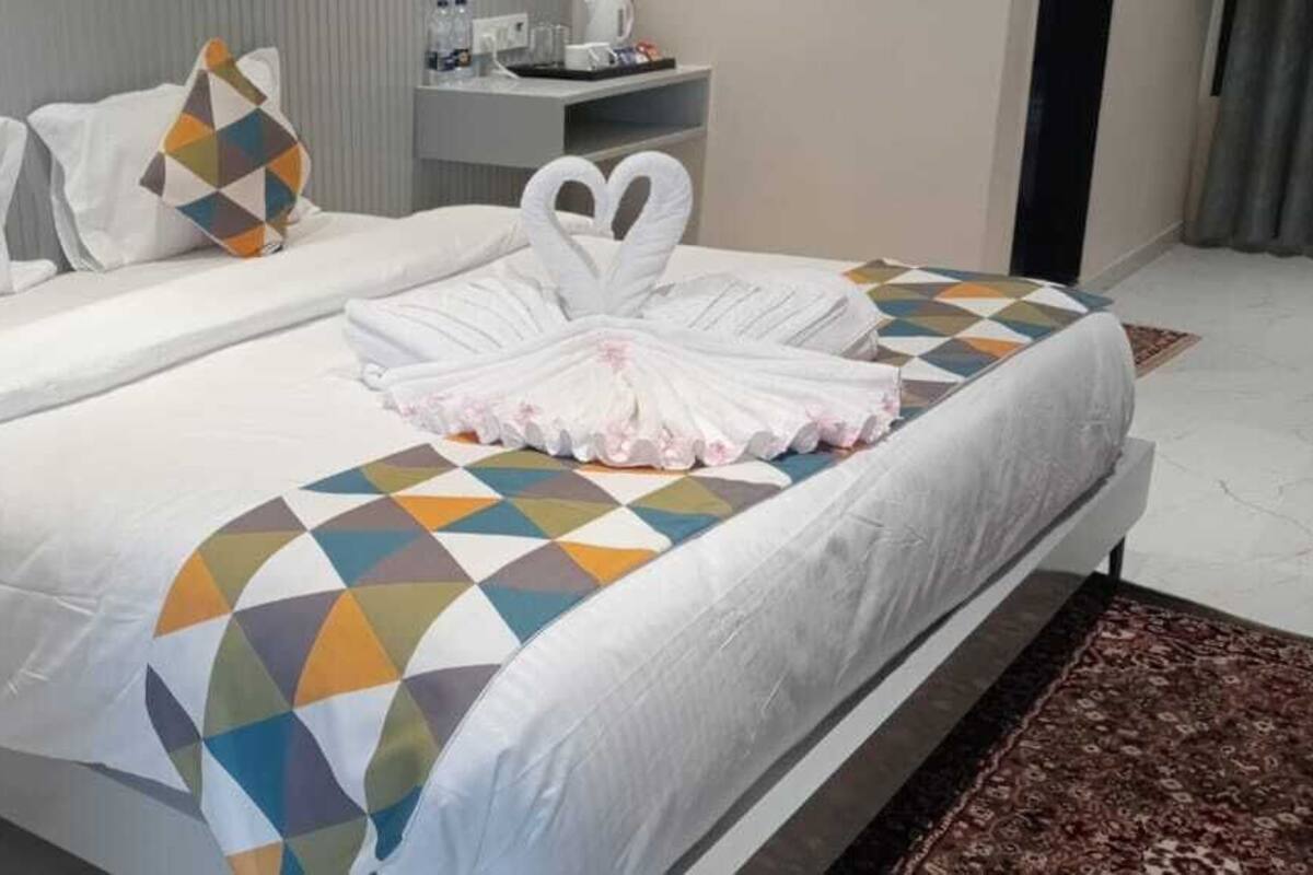 A hotel room with a bed, pillows, a bedside table, and a rug.