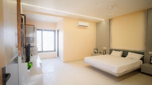 A modern hotel room with a large bed, bedside tables, an air conditioning unit, and a window with blinds.