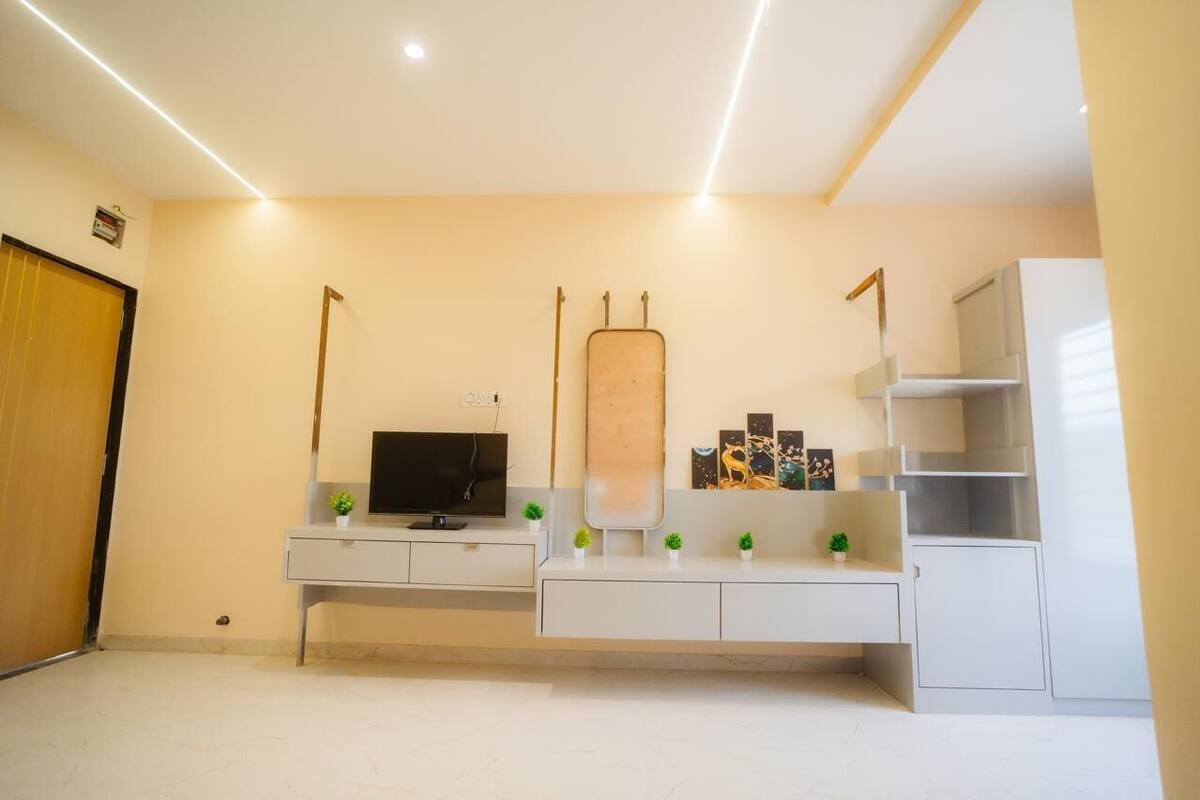 A modern living room with a flat-screen TV, a large mirror, and a minimalist shelving unit.