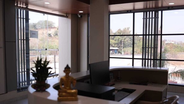 A reception desk with a Buddha statue, a computer, and a chair in a modern office with large windows.