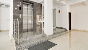 Un ascensor moderno con pared de mármol, barandilla metálica, puerta de vidrio y señal de alarma contra incendios.