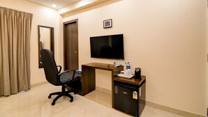 Habitación de hotel con escritorio, silla, televisor y un refrigerador pequeño.