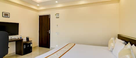 Una habitación de hotel con cama, escritorio, silla, televisor y puerta.