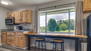 A kitchen with wooden cabinets, a built-in microwave, a window with a view of trees, and two bar stools.