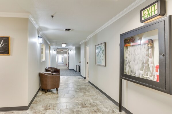 A hotel hallway with a brown leather chair, a framed picture on the wall, and an exit sign.
