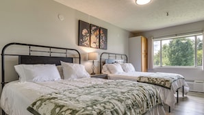 A bedroom with two beds, a nightstand, a lamp, and a window with a view of trees.