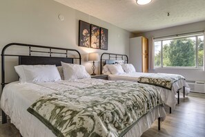 A bedroom with two beds, a nightstand, a lamp, and a window with a view of trees.