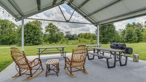 An outdoor patio with picnic tables, rocking chairs, and a barbecue grill.