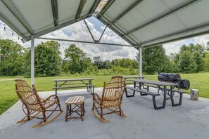 An outdoor patio with picnic tables, rocking chairs, and a barbecue grill.