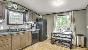 Une cuisine avec des meubles de rangement en bois, un réfrigérateur en acier inoxydable, un évier et une fenêtre avec des rideaux.