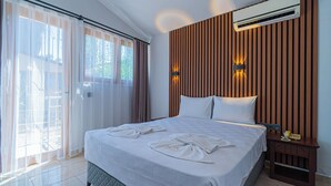 Habitación de hotel con cama, mesita de noche, aire acondicionado y vistas al exterior a través de una ventana con cortinas.