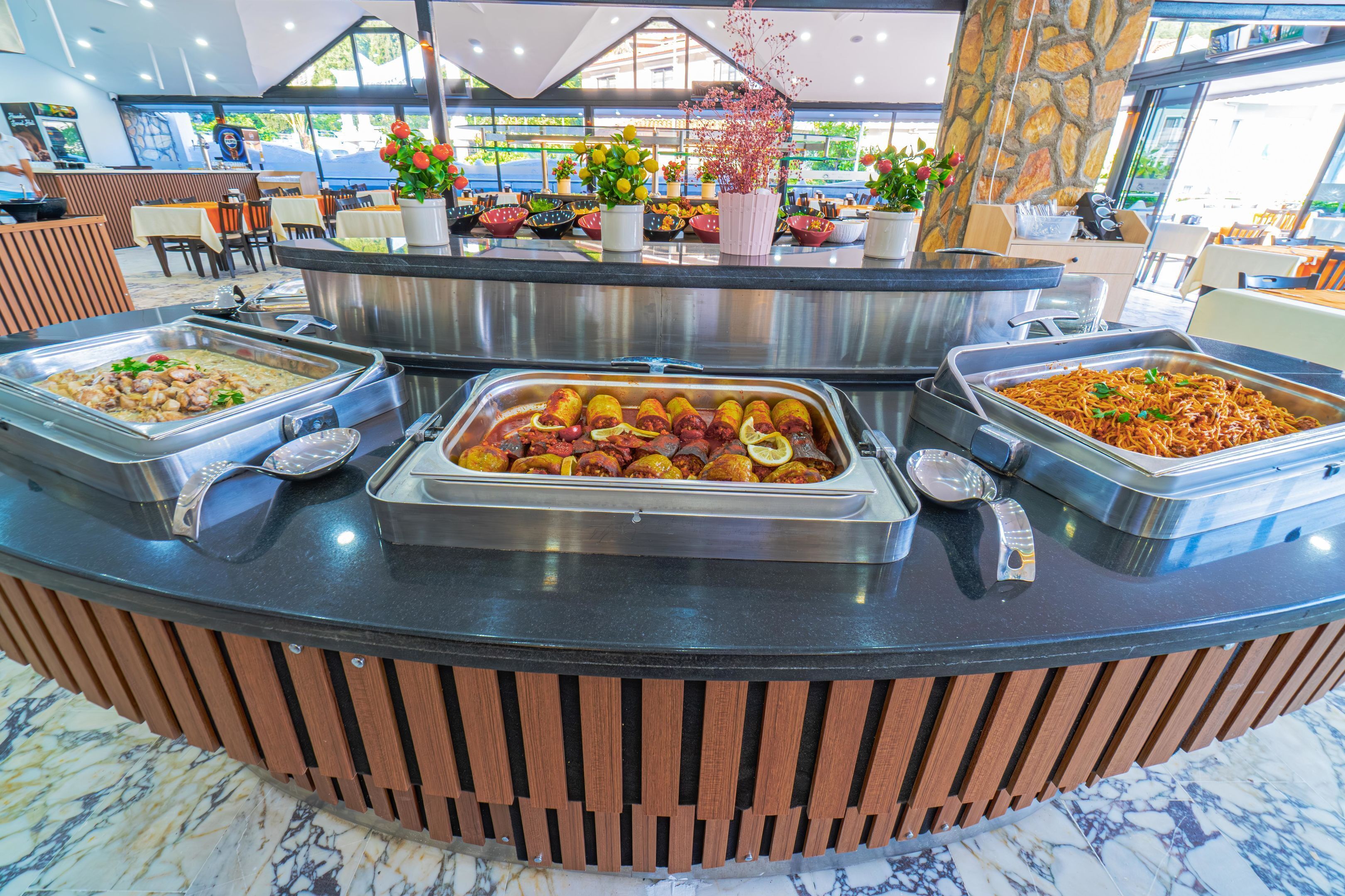 Un mostrador de buffet con diversas opciones de comida, un pilar de piedra y plantas en macetas.