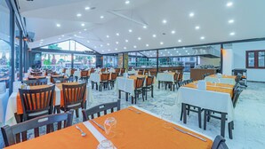 Un restaurante espacioso con numerosas mesas y sillas, amplias ventanas que ofrecen vistas al exterior, y un diseño de techo moderno con iluminación empotrada.