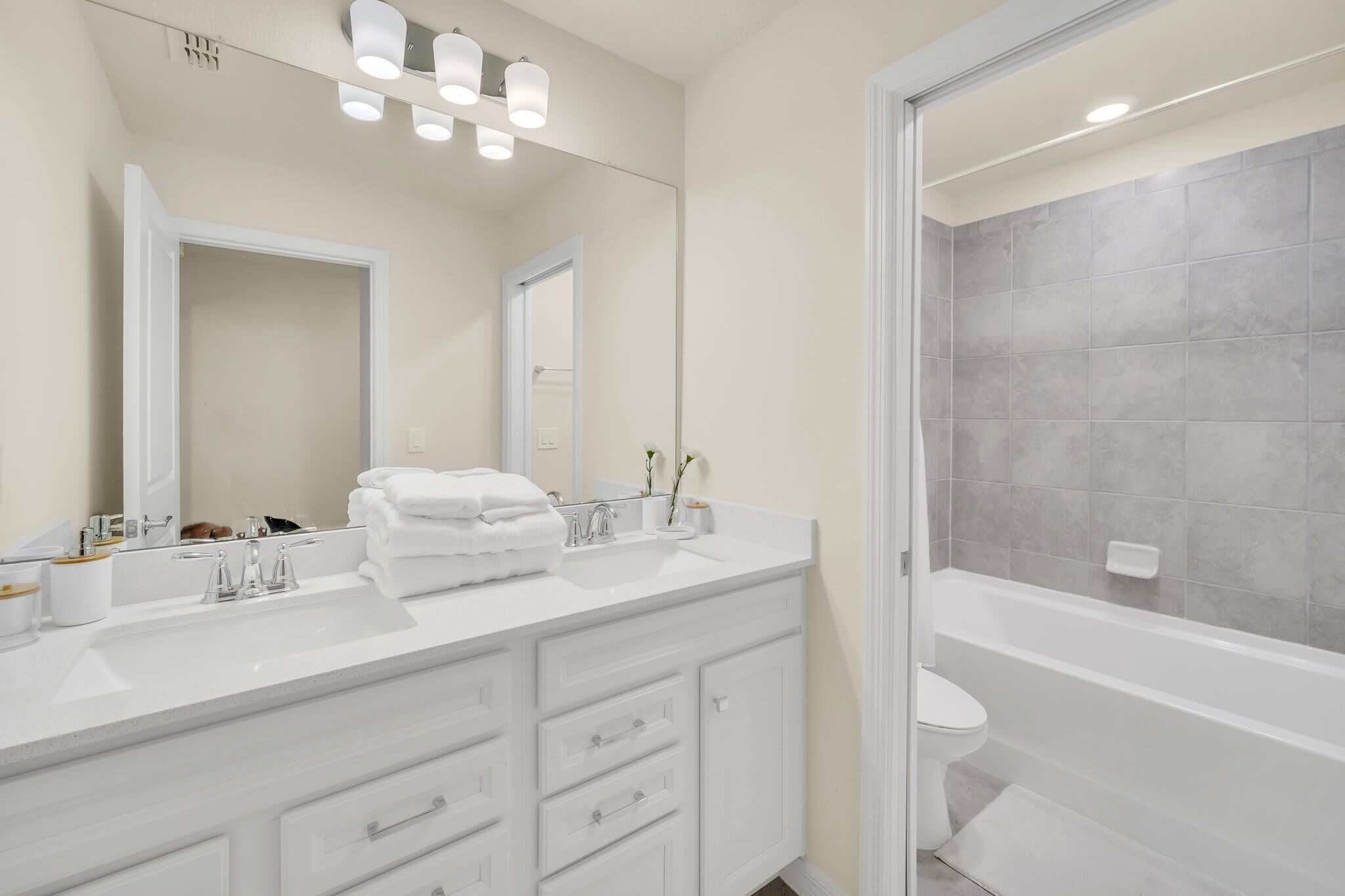 Un bagno moderno con un mobile lavabo bianco, uno specchio grande e una vasca da bagno.