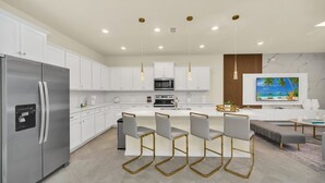Een moderne keuken met witte kastjes, roestvrijstalen apparatuur en een centraal eiland met barstoelen.