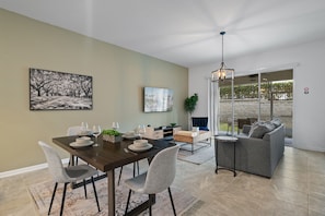 A dining area with a dark wooden table set for four, surrounded by grey chairs. A television is mounted on the wall above the table. - CONDO 2bed-2bath next to Disney - Free Water Park (Kissimmee)