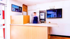 Un comptoir d’accueil avec un revêtement en bois, un écran numérique et un panneau indiquant l’emplacement du bureau et de la salle de repos du personnel.