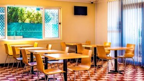 Un espace repas avec des tables et des chaises, une fenêtre donnant sur un paysage verdoyant et un téléviseur fixé au mur.