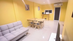 Ein Zimmer mit einer Couch, einem Esstisch mit Stühlen, einem Fernseher und einer Mikrowelle.