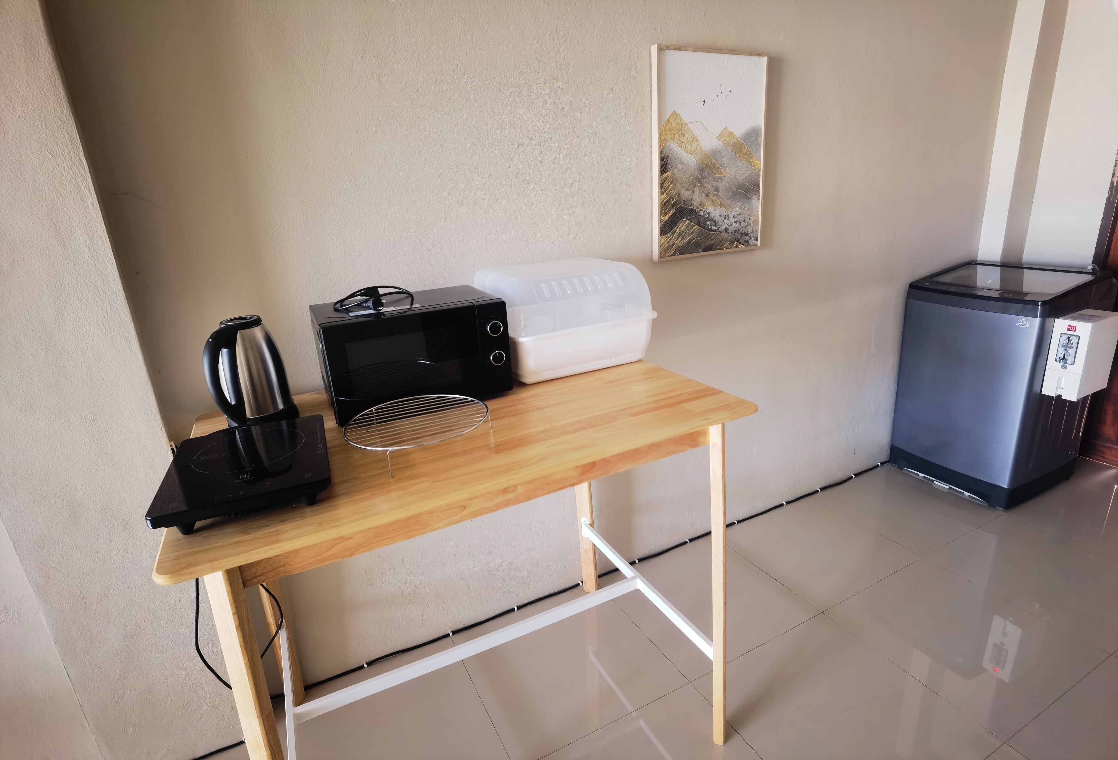 Una pequeña cocina americana con microondas, hervidor y tostadora sobre una mesa de madera.
