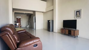 Ein geräumiges Wohnzimmer mit einem braunen Ledersofa, einem Flachbildfernseher auf einem Holzboden und einem Kühlschrank.
