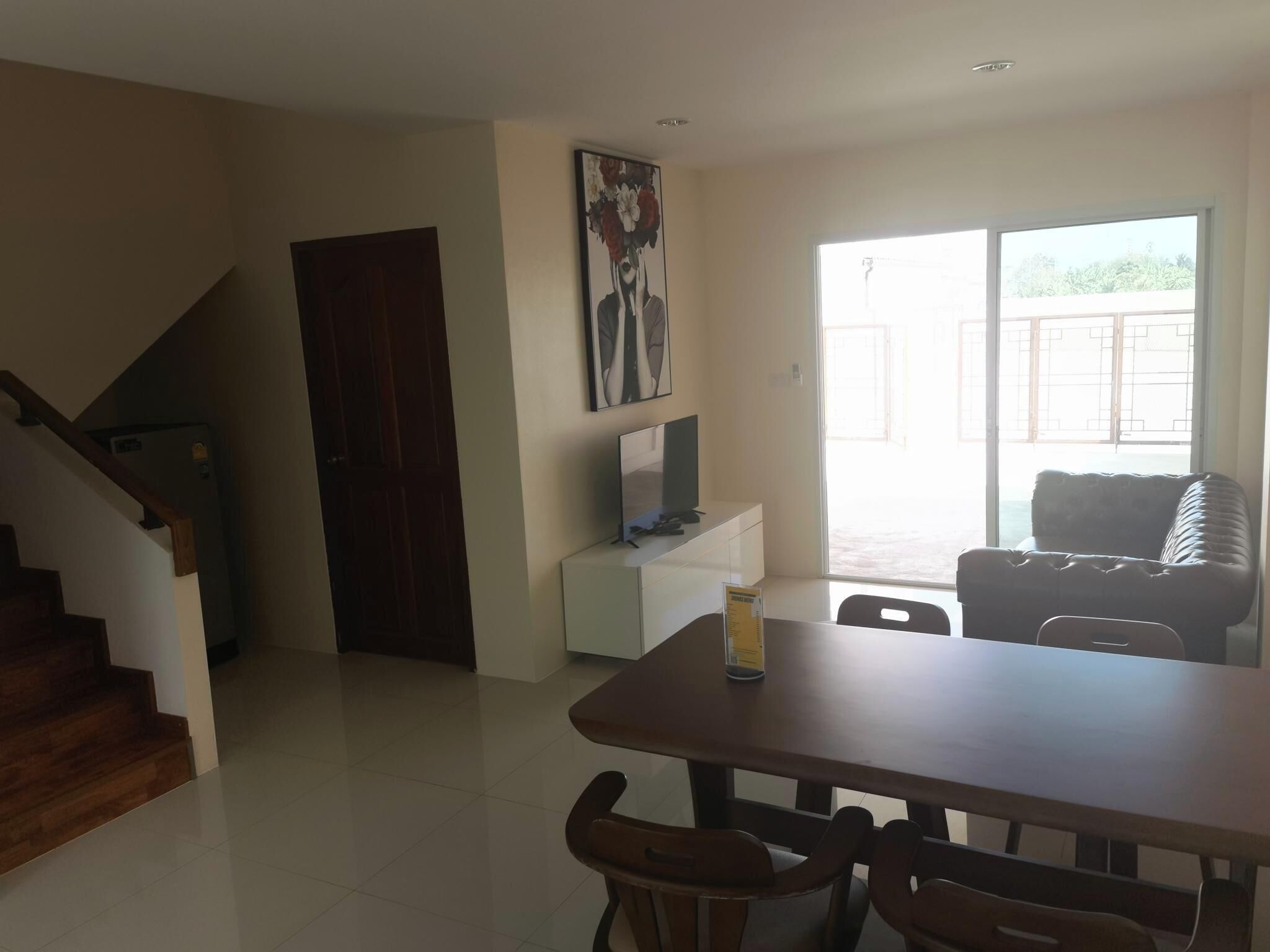 A dining area with a wooden table and chairs, a TV on a white cabinet, and a painting on the wall.