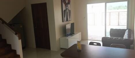 Un coin repas avec une table et des chaises en bois, un téléviseur posé sur un meuble blanc et un tableau accroché au mur.