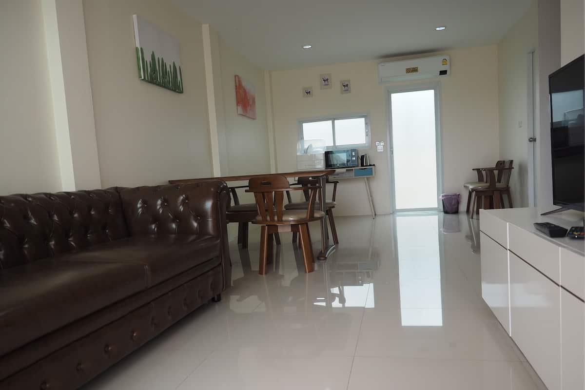 Una sala de estar moderna con un sofá de cuero marrón, una mesa de comedor de madera y sillas. Hay una zona de cocina con un microondas y una ventana.