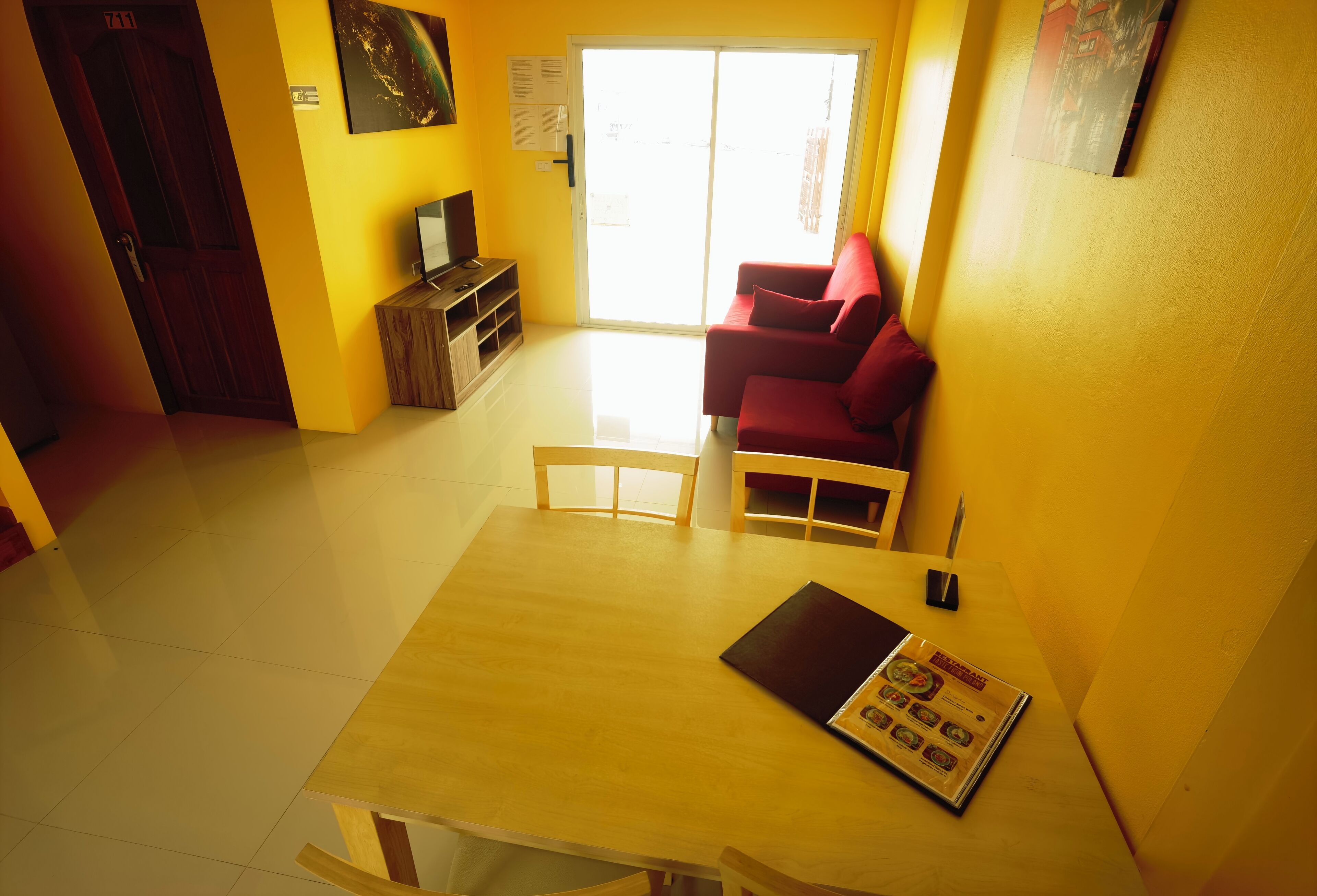 A bright room with a wooden table, a red sofa, and a TV on a wooden cabinet.