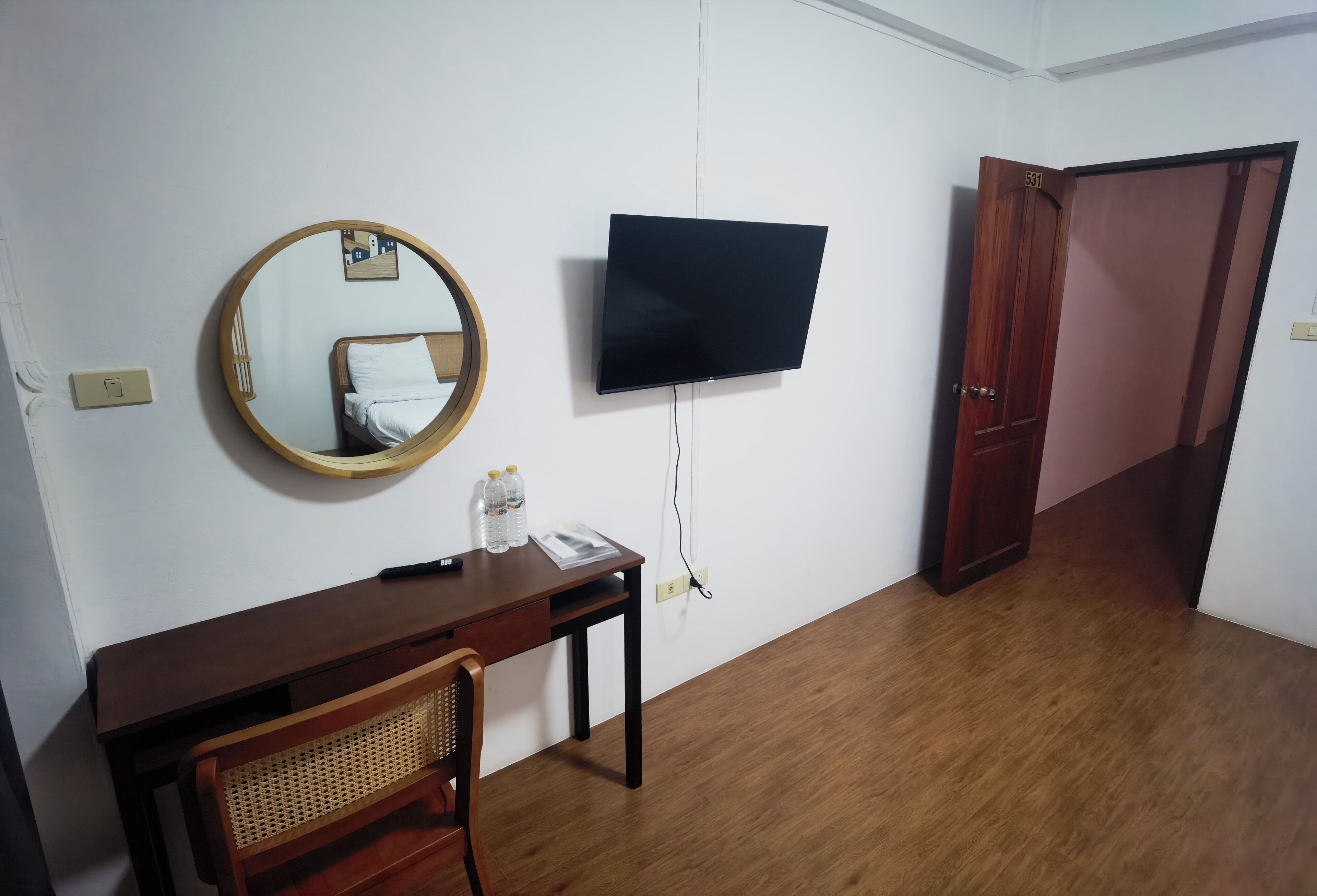 Een kamer met een houten bureau, een ronde spiegel, een flatscreen televisie en een kledingkast.