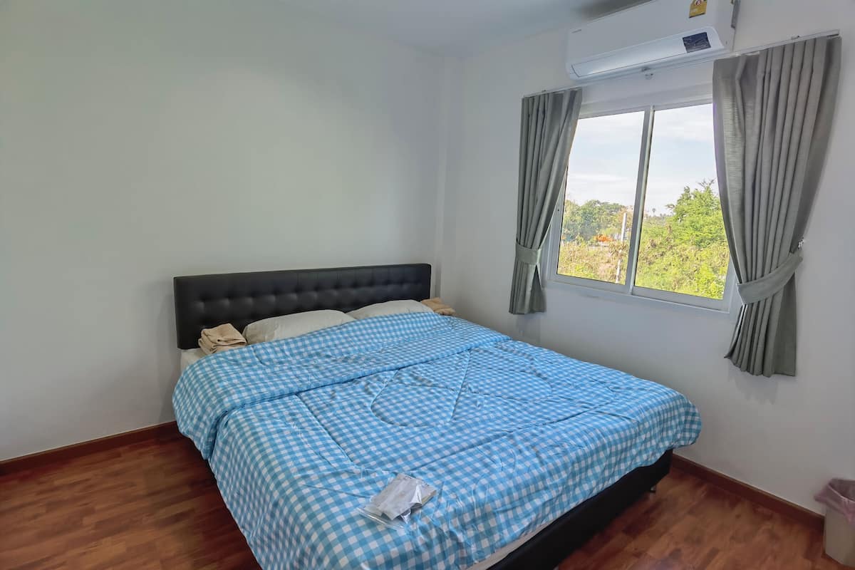 Un dormitorio con cama, ventana con cortinas y unidad de aire acondicionado.