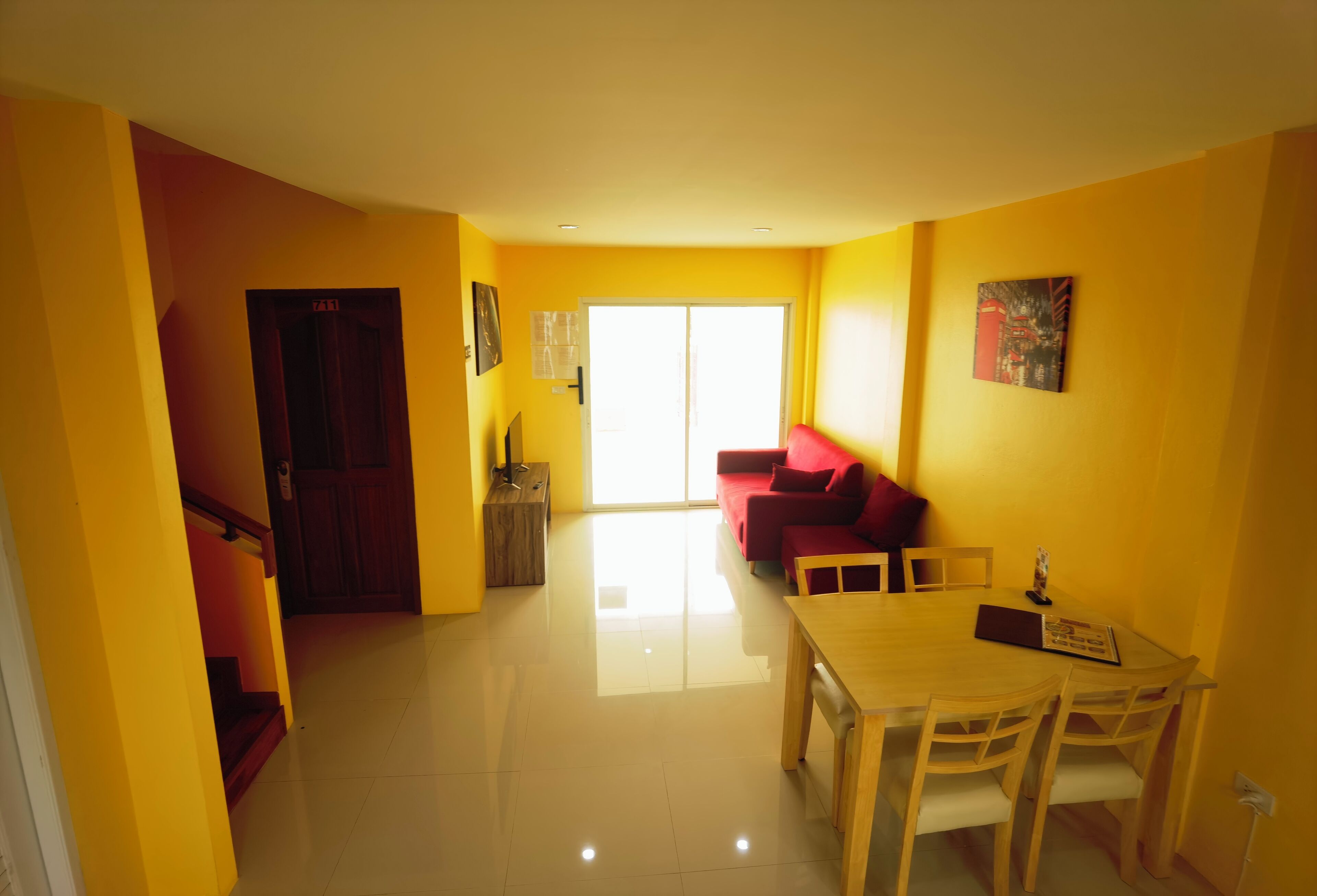 Un salón luminoso con un sofá rojo, una mesa de comedor de madera y una escalera que conduce a otra habitación.