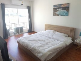 Un dormitorio con cabecera de madera, una cama grande con ropa de cama blanca, un cuadro en la pared y vistas al exterior a través de una ventana con cortinas.