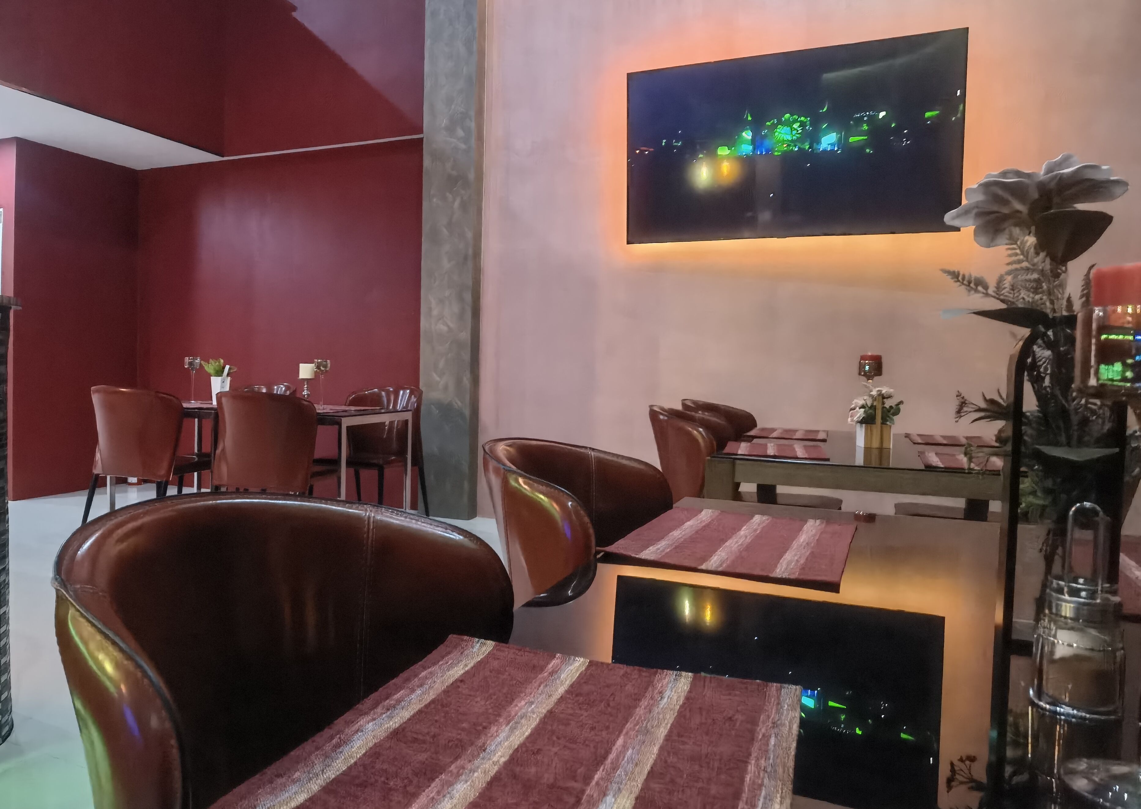 A restaurant with red walls, leather chairs, and a flat-screen TV mounted on the wall.